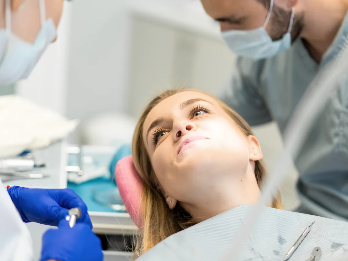 Patientin auf dem Behandlungsstuhl, zwei Behandelnde bereiten die Behandlung vor